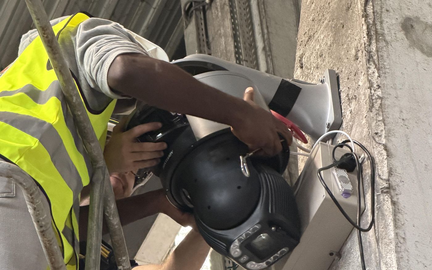 Fixation d'une caméra dôme motorisée et de son boîtier de traitement sur un pilier, au-dessus d'une zone de déchargement.